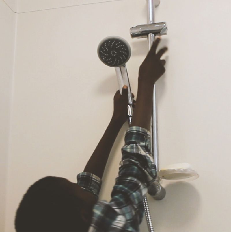En pojke tar ner duschmunstycket från väggen