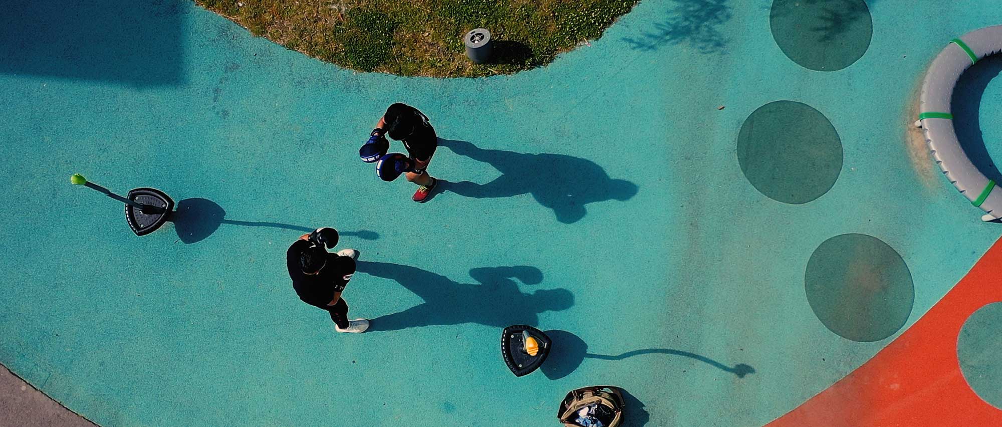 Bild ovanifrån, två personer boxas på en lekplats med blått underlag.