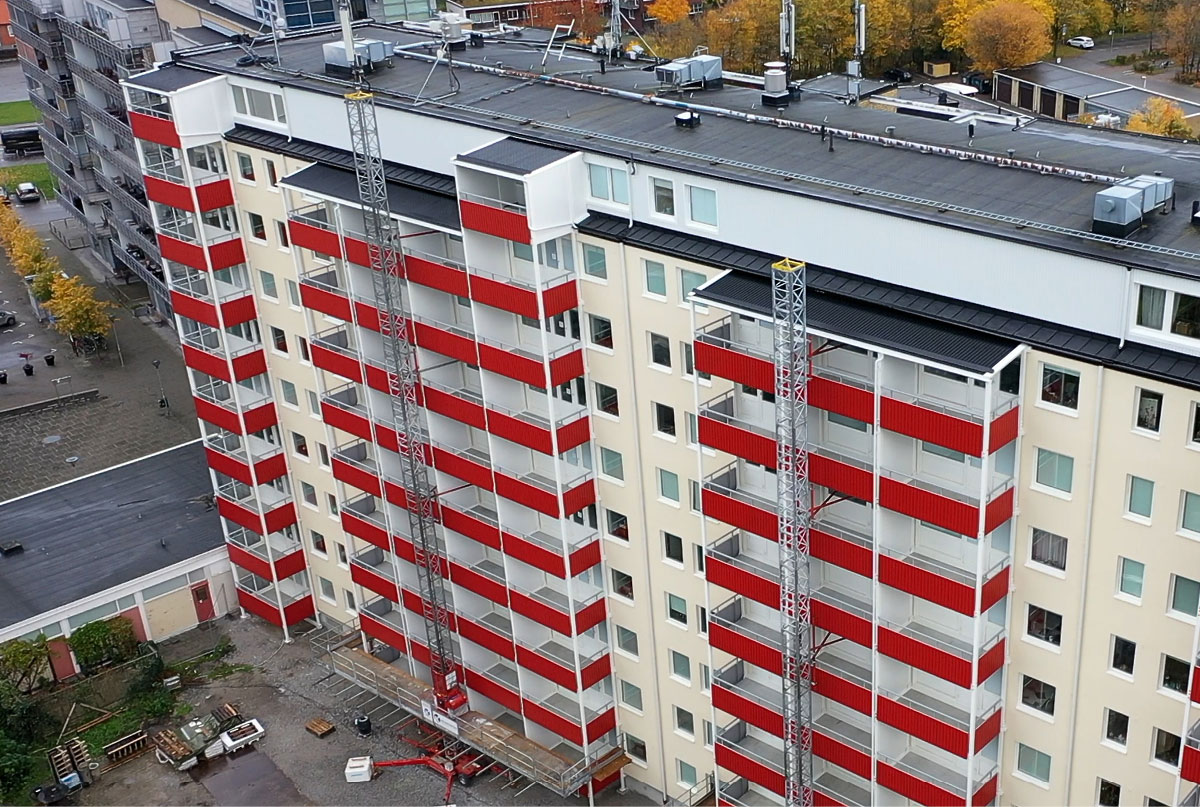 Närbild högt och vitt flervåningshus med röda balkonger och någon byggställning kvar.