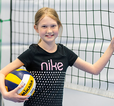 Porträttbild på Tindra med ett volleybollnät i bakgrunden. Hon håller i en volleyboll i ena handen och stödjer sig mot volleybollnätet med den andra.
